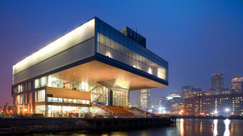 A modern structure with windows overlooking the water lit up at night.