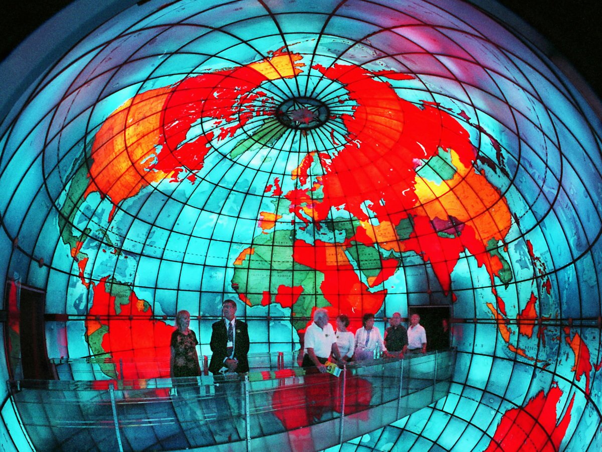 People standing on a bridge inside a colorful stained-glass globe showing the continents.